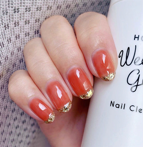Glossy bright orange gel nails with glittery gold thin french nail design. Holding Weekly Gel Nail Cleanser